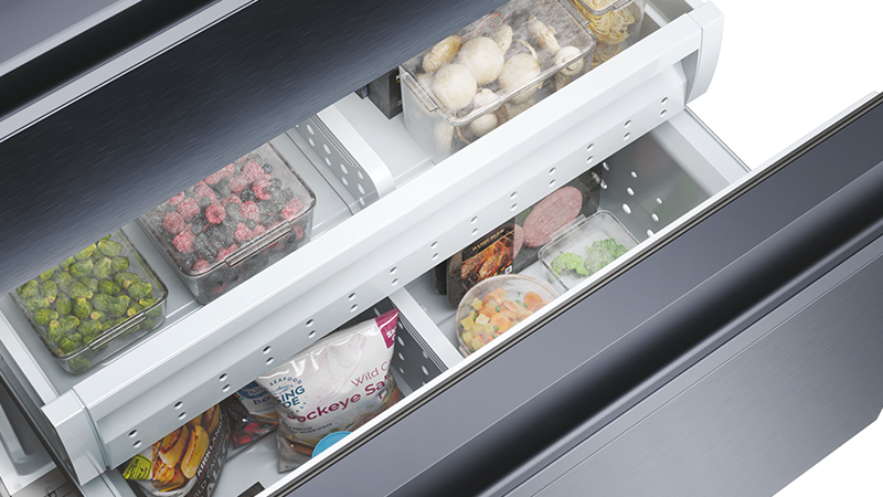 Interno di un cassetto freezer organizzato con funghi, verdure, frutti di bosco, carne confezionata e sacchetti di alimenti surgelati.