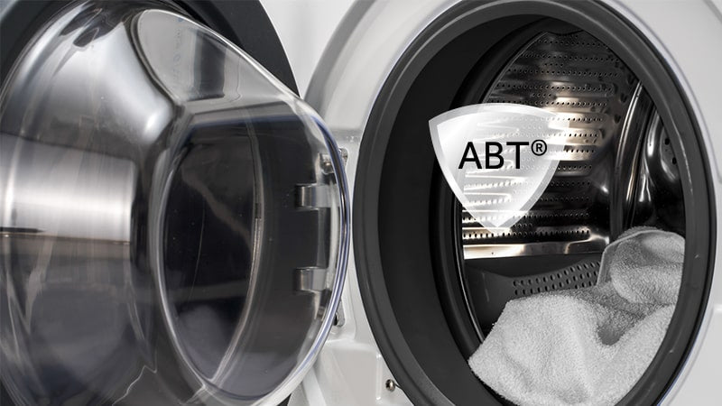 Focus cestello aperto della lavatrice. Sovrapposto c'è un badge con scritto ABT, la funzione anti batterica. 