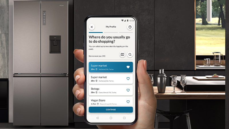 Telefono con aperta l'app hOn, L’Intelligenza Artificiale di Haier, grazie alla geolocalizzazione dei tuoi supermercati preferiti, ti permette di avere la giusta temperatura, all’interno del frigorifero ogni volta che torni dalla spesa.