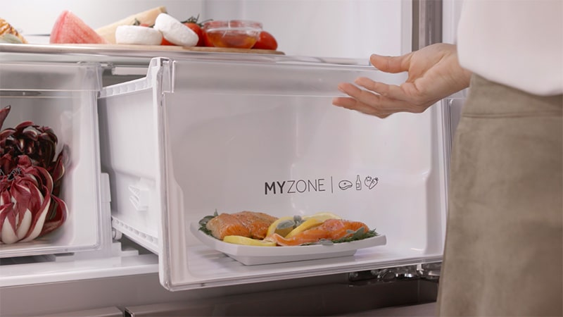 Cassetto del frigorifero con scritta: Myzone in cui si possono inserire alimenti freschi da conservare. Dentro al cassetto c'è un piatto di salmone con degli spicchi di limone. 