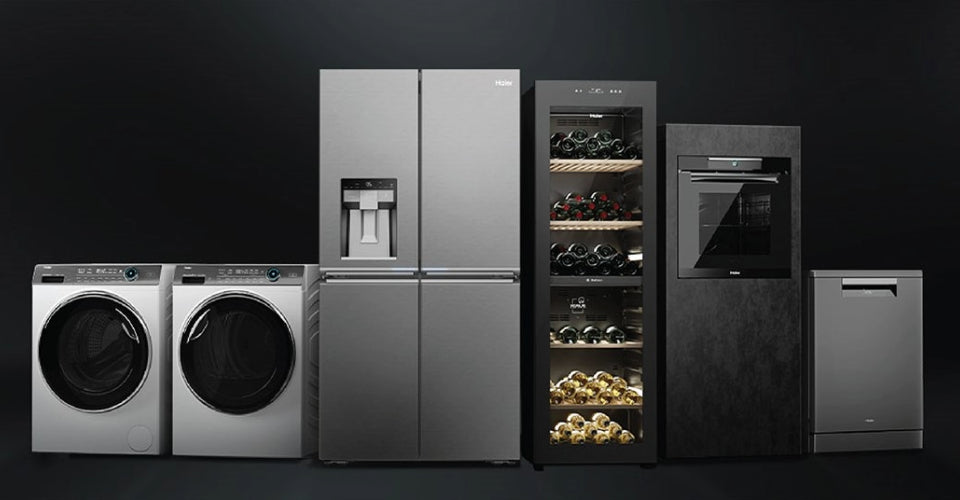 Linea di elettrodomestici Haier su sfondo nero: lavatrice e asciugatrice a carica frontale, frigorifero con dispenser ghiaccio, cantinetta vino, forno con comandi digitali e lavastoviglie
