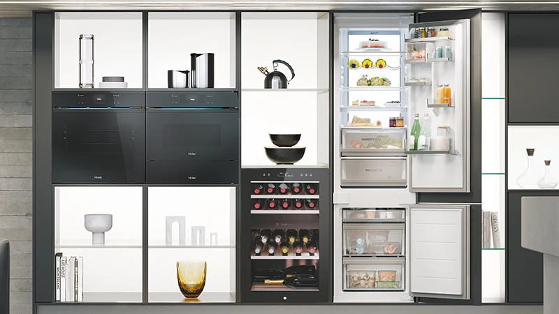Cucina moderna con elettrodomestici Haier: forno, microonde, frigorifero aperto con cibi all’interno e cantinetta vino con bottiglie visibili.