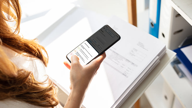 Persona che consulta uno smartphone e dei documenti, in un contesto lavorativo o domestico