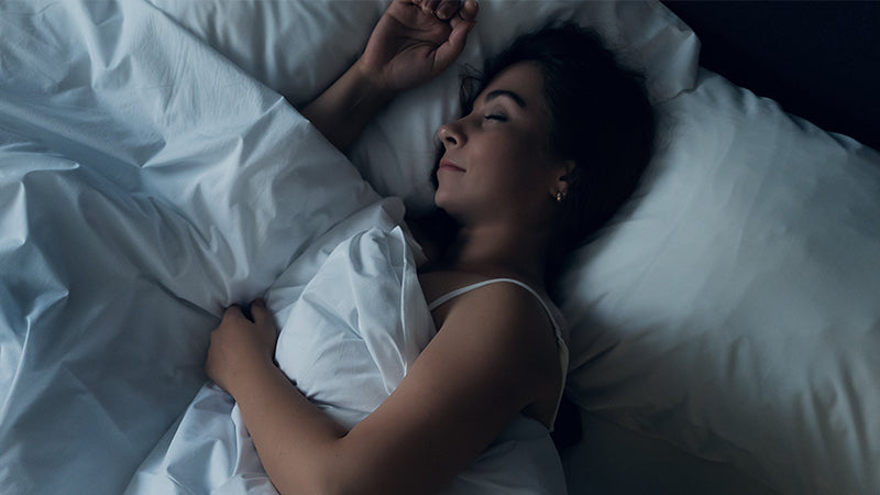 Persona che dorme in un letto con lenzuola bianche, ambiente scuro e rilassante
