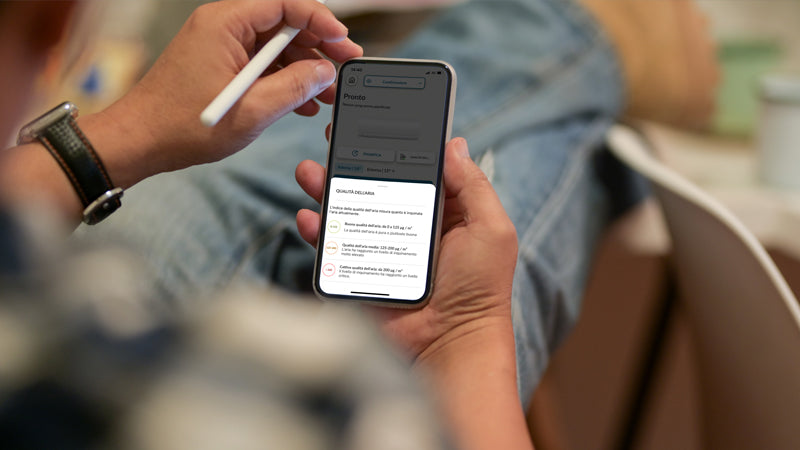 Persona tiene uno smartphone con schermata di notifiche dell'app Haier, in un ambiente domestico informale