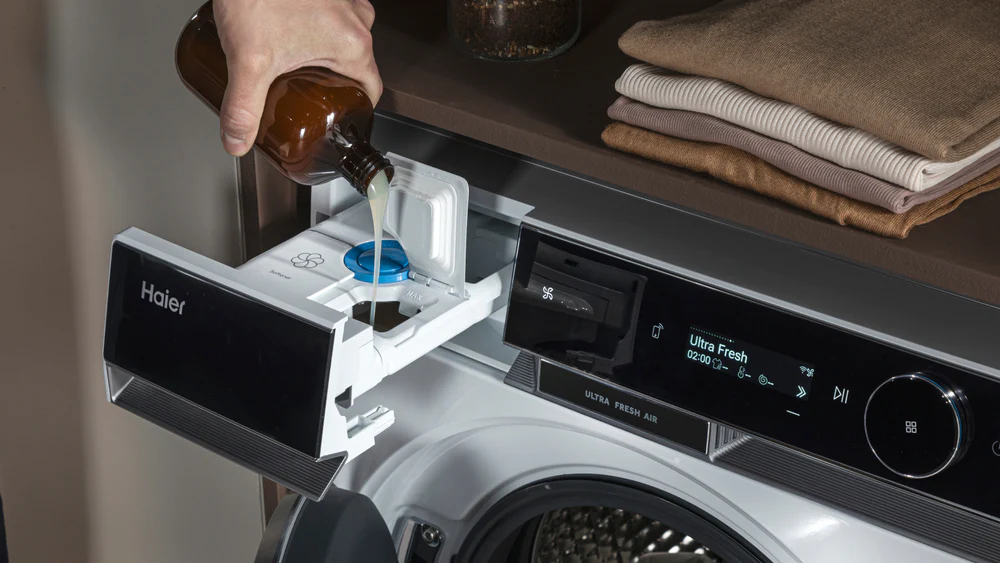 Dettaglio di una mano che versa detersivo liquido nel cassetto di una lavatrice.