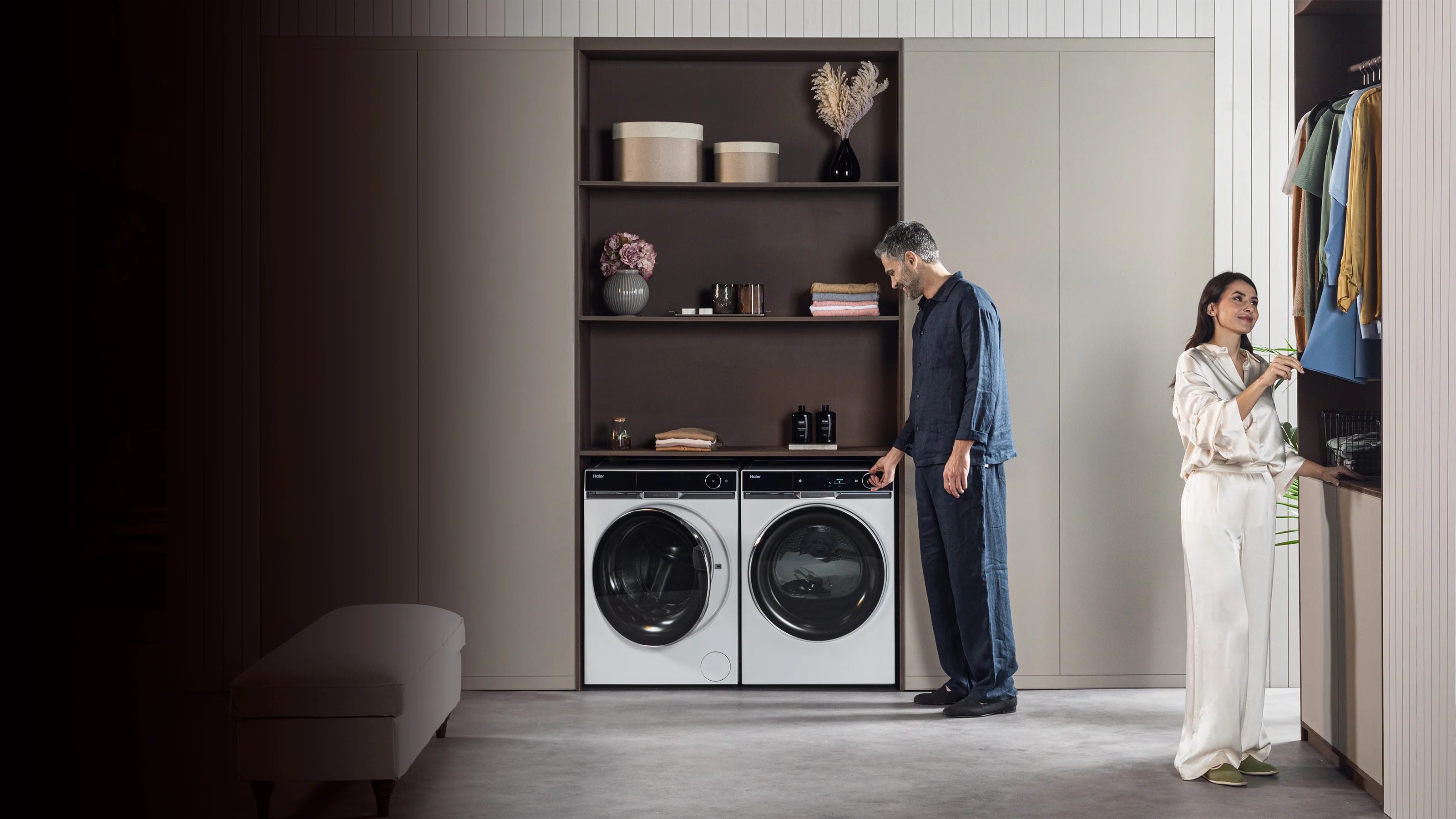 Lavatrice e asciugatrice posti in un mobile dentro una camera da letto. Accanto ai due elettrodomestici c'è un armadio con una donna e un uomo.