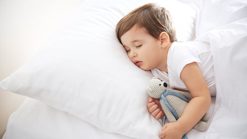 Bambino che dorme sul letto con un peluche in mano.