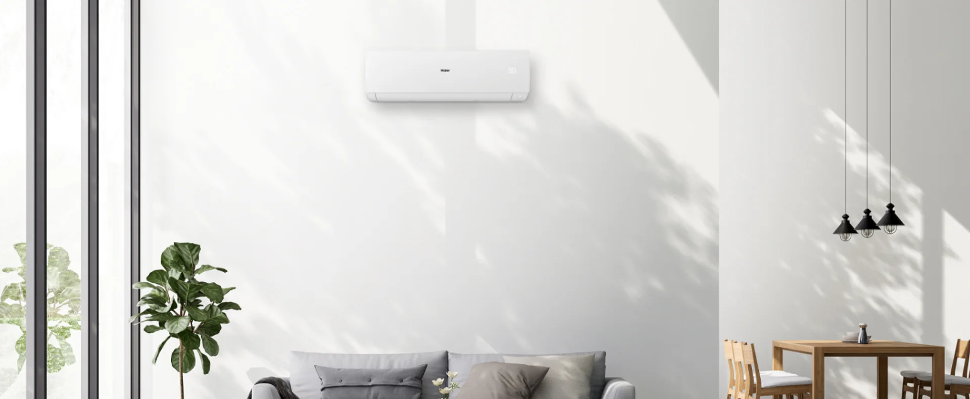 Condizionatore Sphera posto all'interno di un salotto. E' appeso al muro e sotto ha un divano con di fianco un tavolo da pranzo e delle lampade stile industriale.
