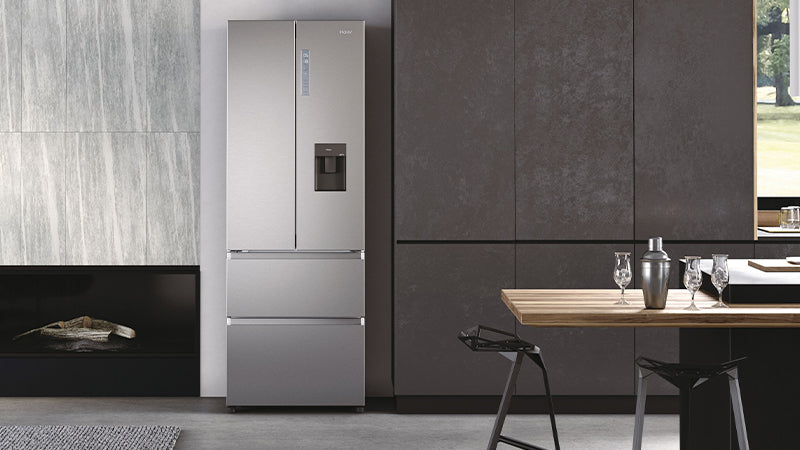 Frigorifero posto tra un camino e un mobile da cucina. Il frigorifero è multidoor inox con scompartimento del ghiaccio. Di fronte al frigorifero c'è un tavolo con lo shaker da cocktail.