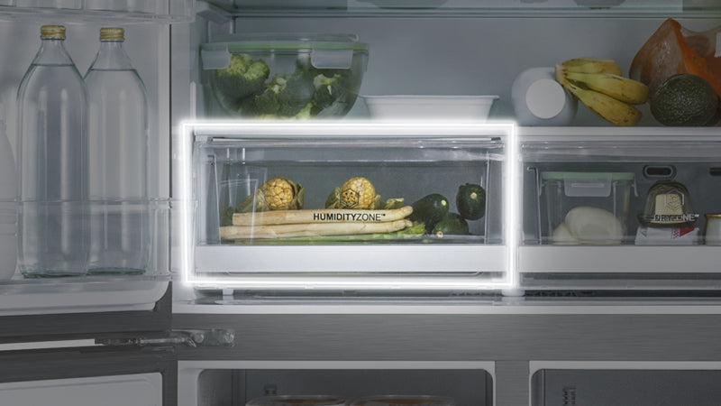 Focus sul cassetto "humidity zone" del frigorifero. Nel cassetto ci sono alimenti freschi come pannocchie, asparagi, zucchine. Negli altri scompartimenti ci sono formaggio, banane, latte, avocado, confezione di carne, broccoli. 