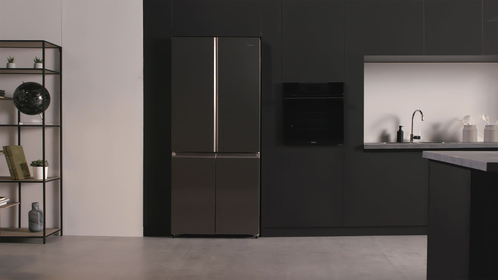 Cucina con focus sul frigorifero inox e sul forno incassato nel muro. Accanto al frigorifero c'è un mobile con un mappamondo e dei libri.