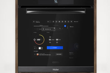 Forno da incasso Chef@Home Haier con porta full touch e interfaccia digitale, integrato in una cucina moderna con pannelli effetto cemento; visibile il display con temperatura impostata, timer e ricette interattive.