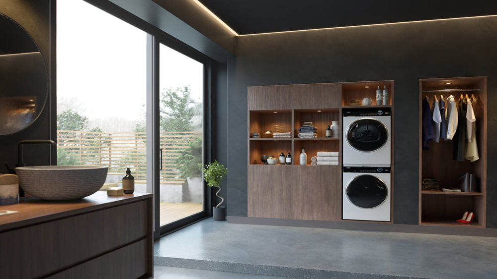 Lavatrice e asciugatrice in colonna inseriti in un armadio a muro all'interno di un bagno. Accanto all'armadio a muro c'è un armadio con i vestiti appesi, scarpe con il tacco e borse.