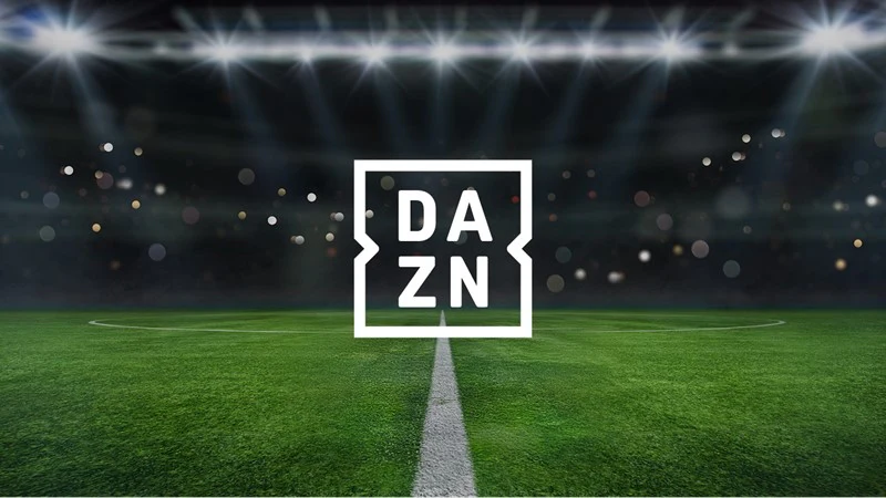 Immagine di un campo da calcio notturno con luci abbaglianti sopra e un logo centrale di DAZN che sovrasta il campo.
