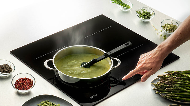 Piano cottura ad induzione Haier Series 4 dove una persona sta cucinando un passato di verdure