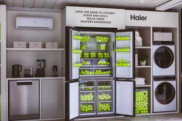 Showroom Haier dotato di lavastoviglie, prodotti KSDA, condizionatore, lavatrice e asciugatrice in colonna e un frigorifero multiporta riempito di palline da tennis.